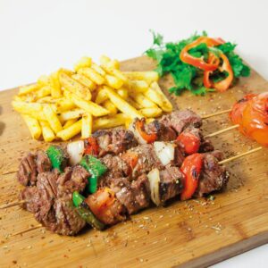 Delicious grilled shashlik served with seasoned french fries and fresh vegetables on a wooden board.