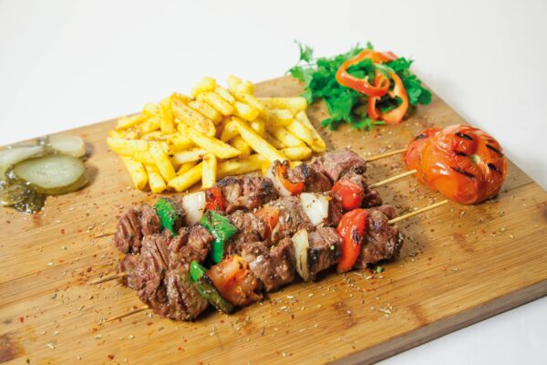 Delicious grilled shashlik served with seasoned french fries and fresh vegetables on a wooden board.