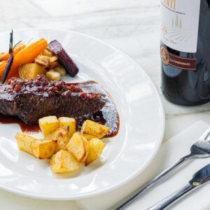 Elegant gourmet meat dish served with vegetables and a glass of red wine.