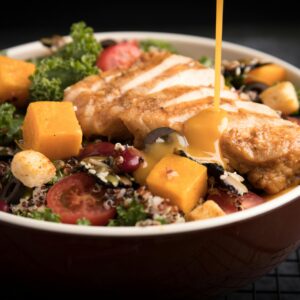 A colorful chicken salad with honey dressing, featuring fresh vegetables and grains.