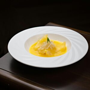 A plated dessert with mango sauce and garnished toppings served on a wooden table.