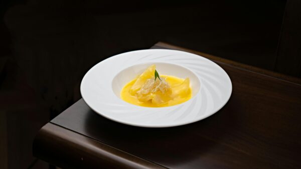 A plated dessert with mango sauce and garnished toppings served on a wooden table.