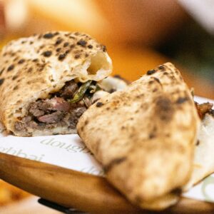 Close-up of a flavorful folded flatbread stuffed with savory ingredients on a wooden board.