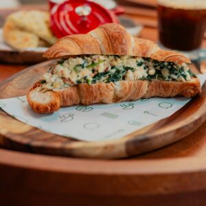 Delicious croissant stuffed with spinach and cheese served on a wooden plate, perfect for a hearty breakfast.