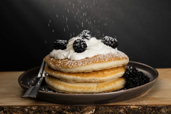Mouthwatering pancakes topped with cream and blackberries, dusted with powdered sugar.