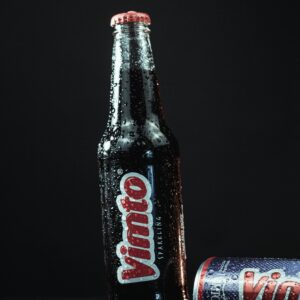 Refreshing Vimto drink bottle and can with water droplets on a dark surface.