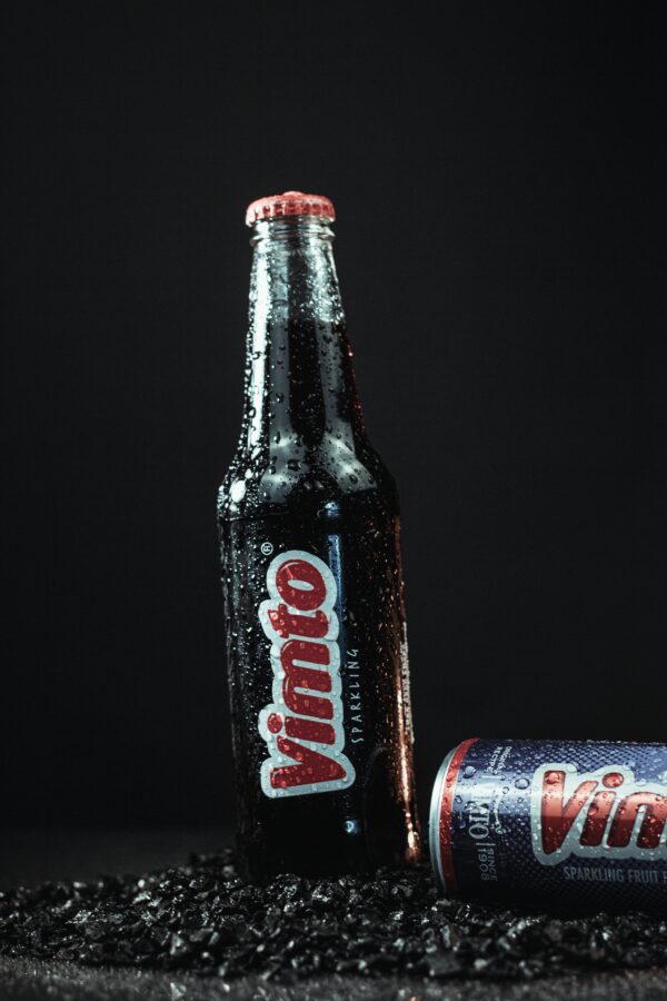 Refreshing Vimto drink bottle and can with water droplets on a dark surface.