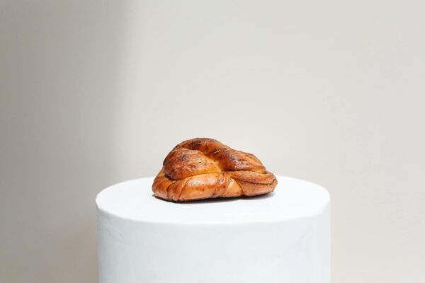 A single cardamom knot bun elegantly presented on a minimalist white pedestal against a neutral background.