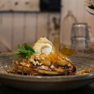 Delicious pancaked with caramel and syrup served on plate with ice cream scoop and decorated with fresh mint leaves in cafe