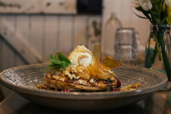 Delicious pancaked with caramel and syrup served on plate with ice cream scoop and decorated with fresh mint leaves in cafe