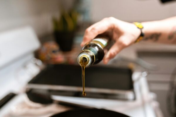 A focused image showing olive oil being poured from a bottle into a pan during cooking.