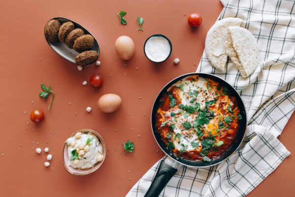Flat lay of Middle Eastern breakfast featuring shakshuka, falafel, pita, and hummus.