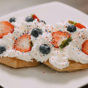 Close-up of waffles topped with strawberries, blueberries, whipped cream, and sprinkles.