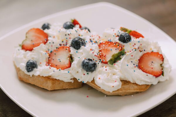Close-up of waffles topped with strawberries, blueberries, whipped cream, and sprinkles.