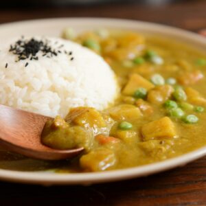 A delicious plate of creamy vegetable curry served with rice and a wooden spoon, perfect for a tasty meal.