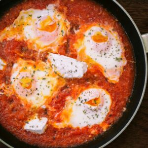 Top view of homemade shakshuka with eggs and herbs in a frying pan.