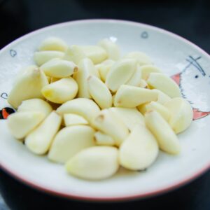 A close-up photo of peeled garlic cloves arranged on a decorative plate, highlighting their freshness.