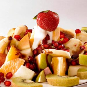 A colorful fruit salad featuring kiwi, strawberry, banana, apple, orange, and pomegranate seeds.