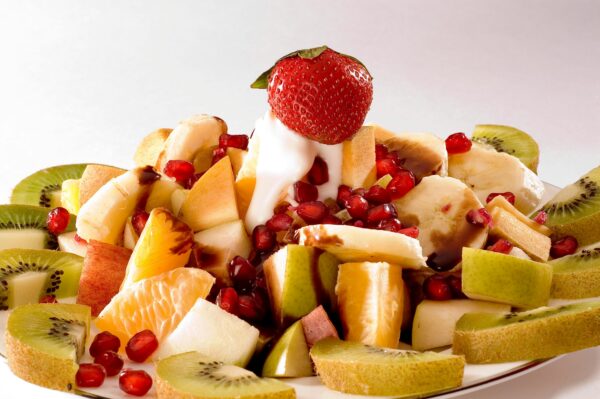 A colorful fruit salad featuring kiwi, strawberry, banana, apple, orange, and pomegranate seeds.