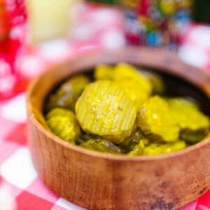 Close-up of pickled cucumbers in a wooden bowl on a red and white checked tablecloth, perfect for food photography.