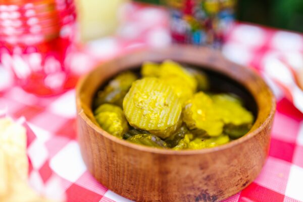 Close-up of pickled cucumbers in a wooden bowl on a red and white checked tablecloth, perfect for food photography.