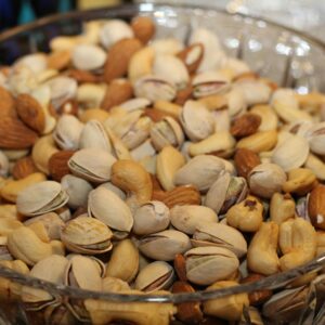 A close-up view of a glass bowl filled with various mixed nuts, including almonds, cashews, and pistachios.