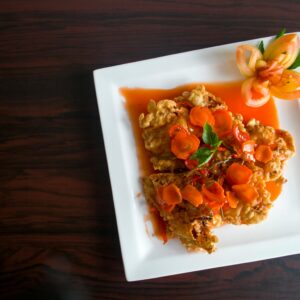 Crispy fried chicken topped with carrots and a floral tomato garnish.